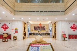 Un hall d’entrée spacieux avec un comptoir d’accueil, une fontaine décorative et des éléments décoratifs rouges sur les murs.