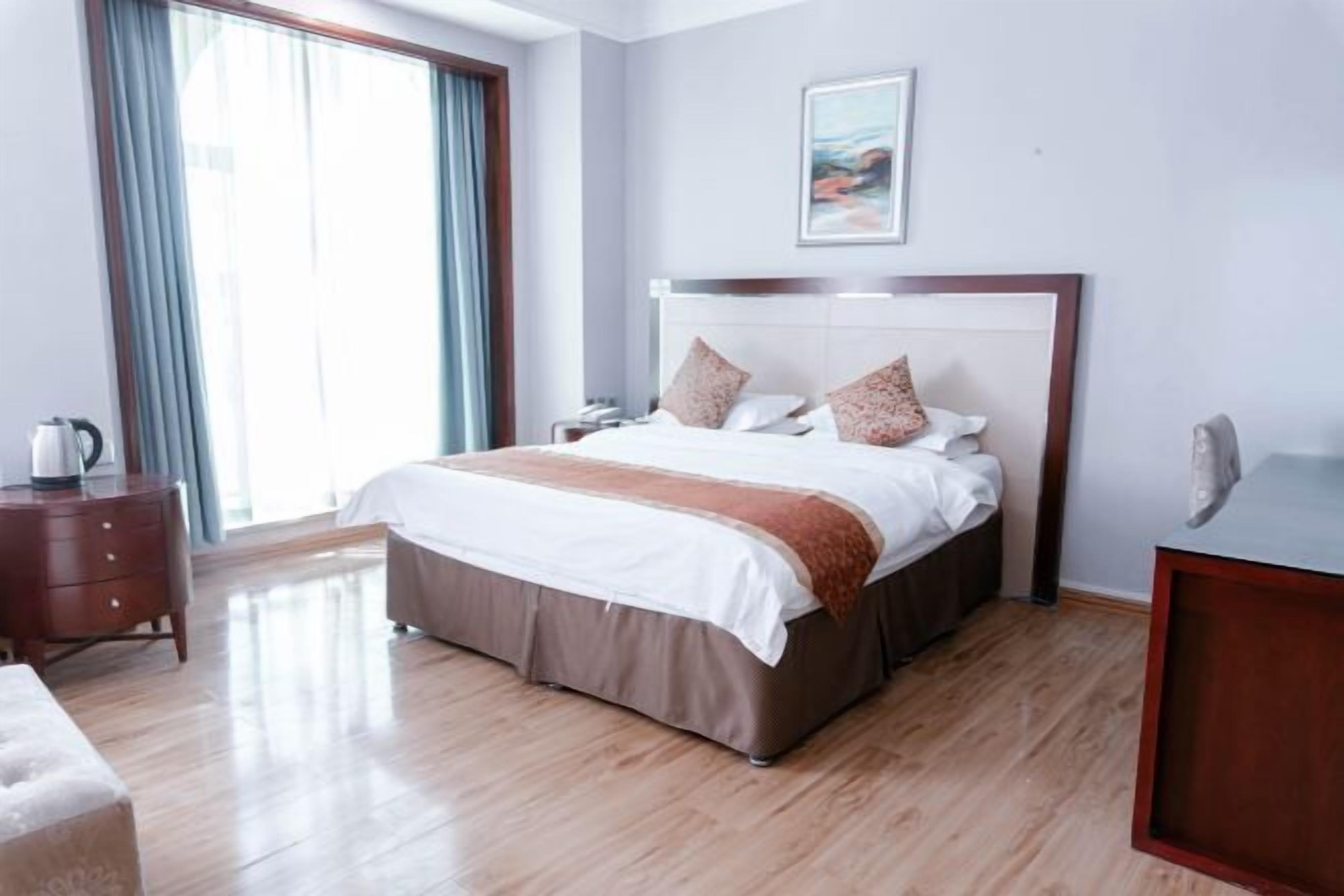 Une chambre d’hôtel avec un grand lit, une table de chevet, une commode et une fenêtre avec des rideaux.
