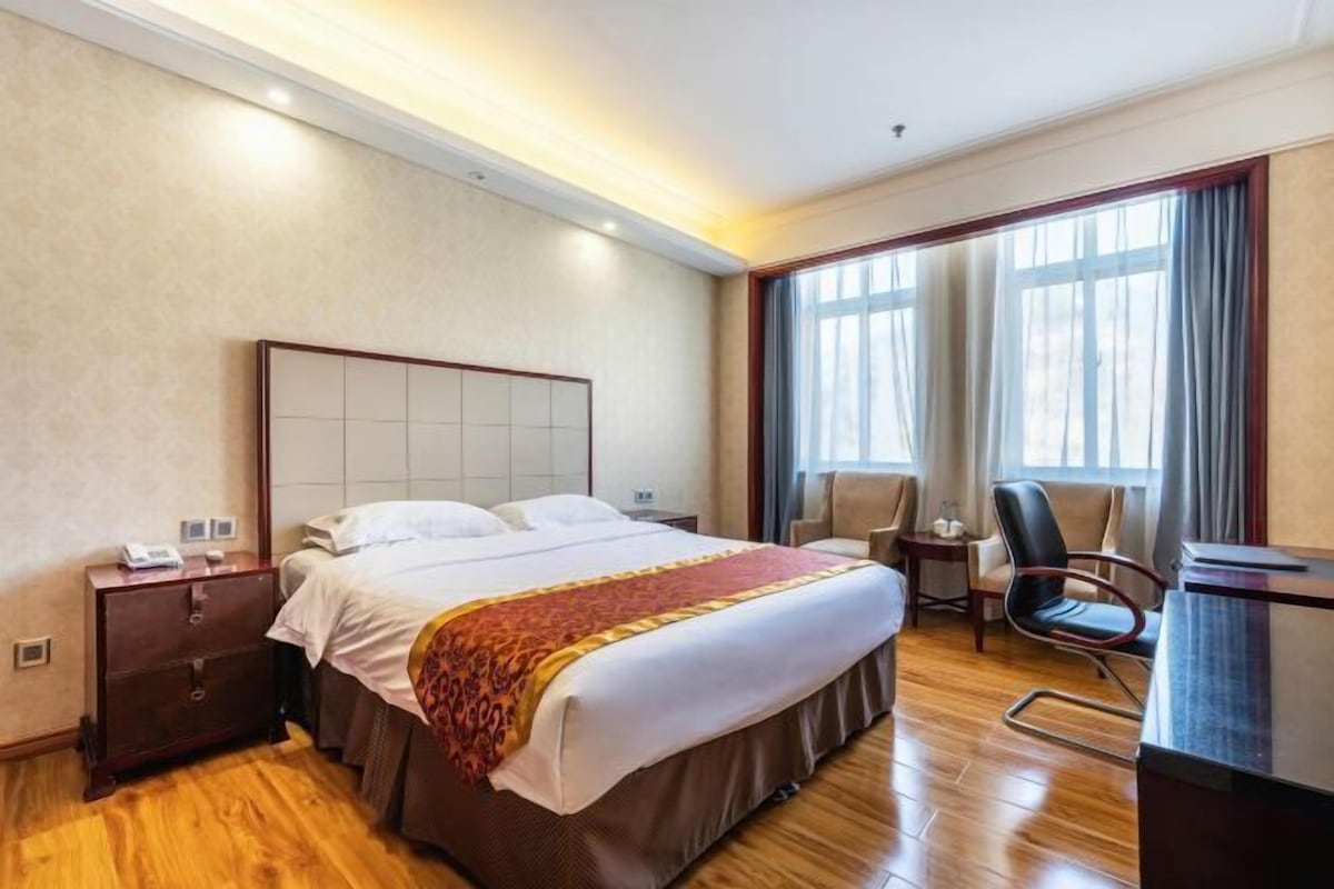 Una habitación de hotel con una cama grande, un escritorio, una silla y una ventana con cortinas.