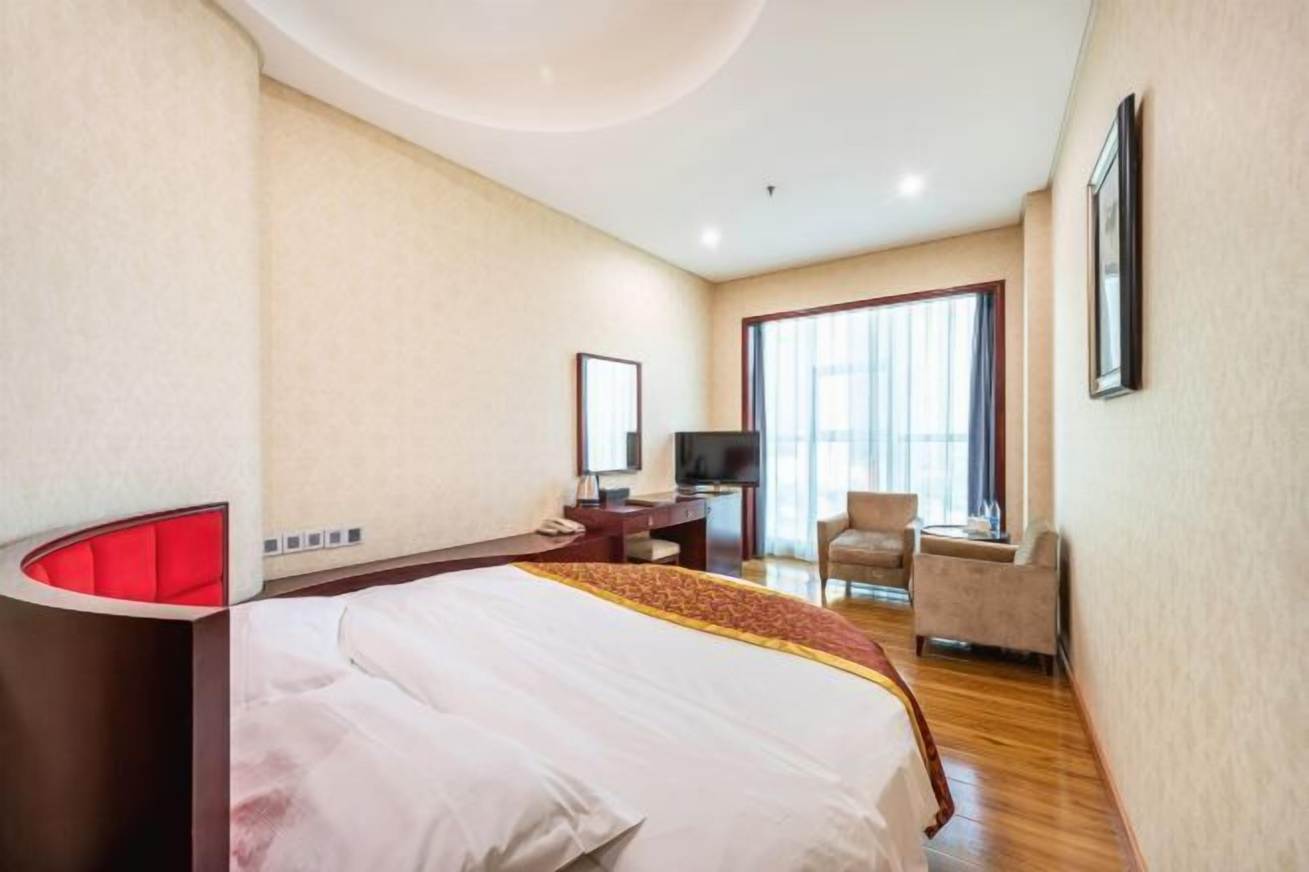 Une chambre d’hôtel avec un grand lit, un bureau avec une chaise, une télévision et une grande fenêtre.