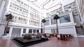 A spacious atrium with a high ceiling, multiple floors of balconies, and a central seating area with tables and chairs.