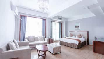 A hotel room with a sofa, ottoman, bed, and a chandelier.