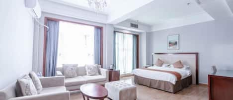 A hotel room with a sofa, ottoman, bed, and a chandelier.
