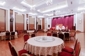 Een balzaal met ronde tafels, stoelen en een podium met rode gordijnen.