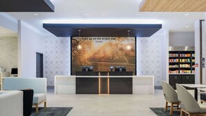 A modern reception area with a large digital screen displaying a scenic image, a reception desk, seating area, and a snack bar.
