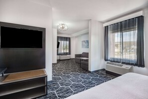 Habitación de hotel con una cama grande, televisión de pantalla plana, sofá y un amplio ventanal con cortinas.