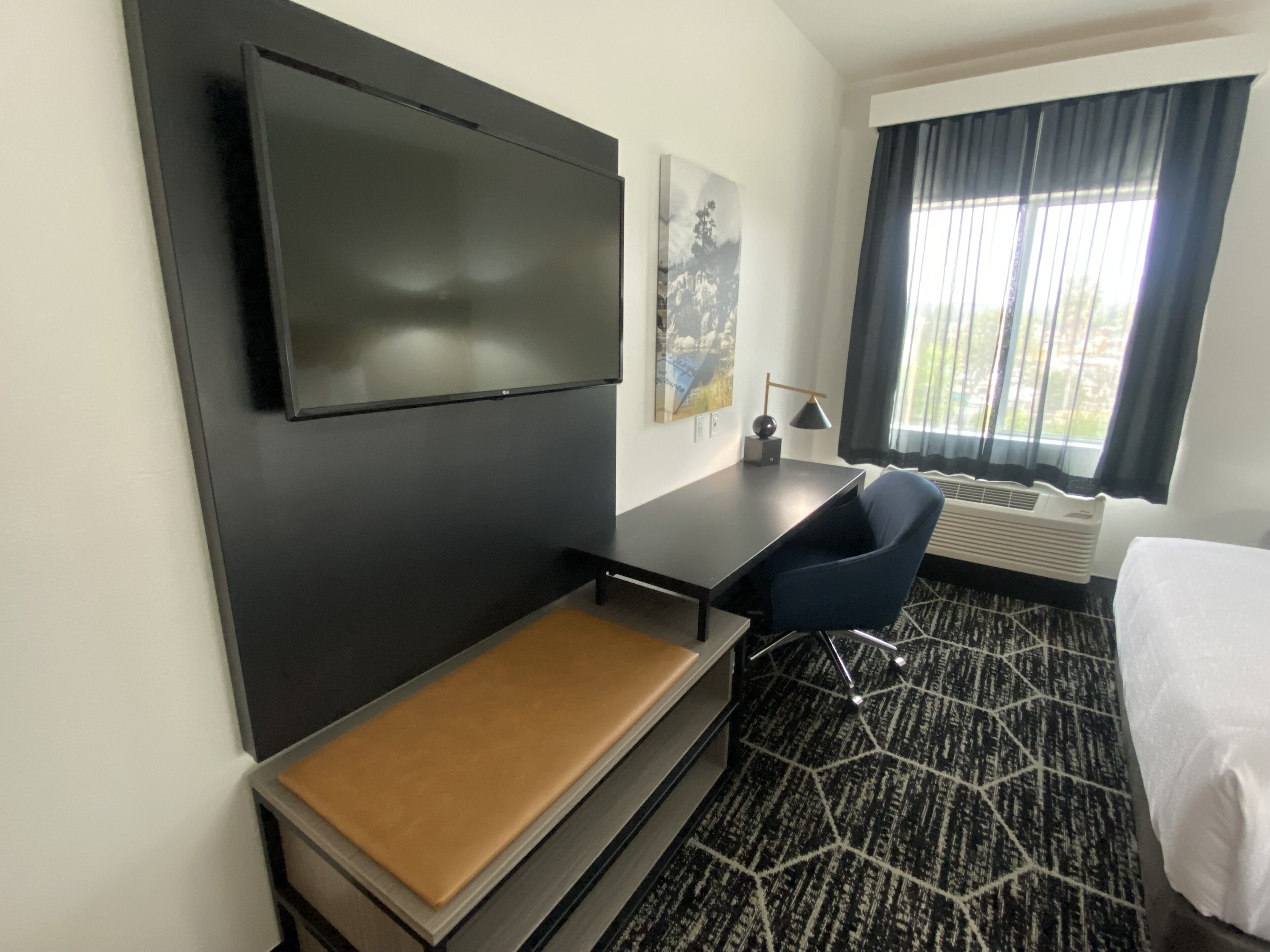 Une chambre d’hôtel équipée d’un téléviseur à écran plat fixé au mur, d’un bureau avec une chaise, d’un lit et d’une fenêtre avec des rideaux.