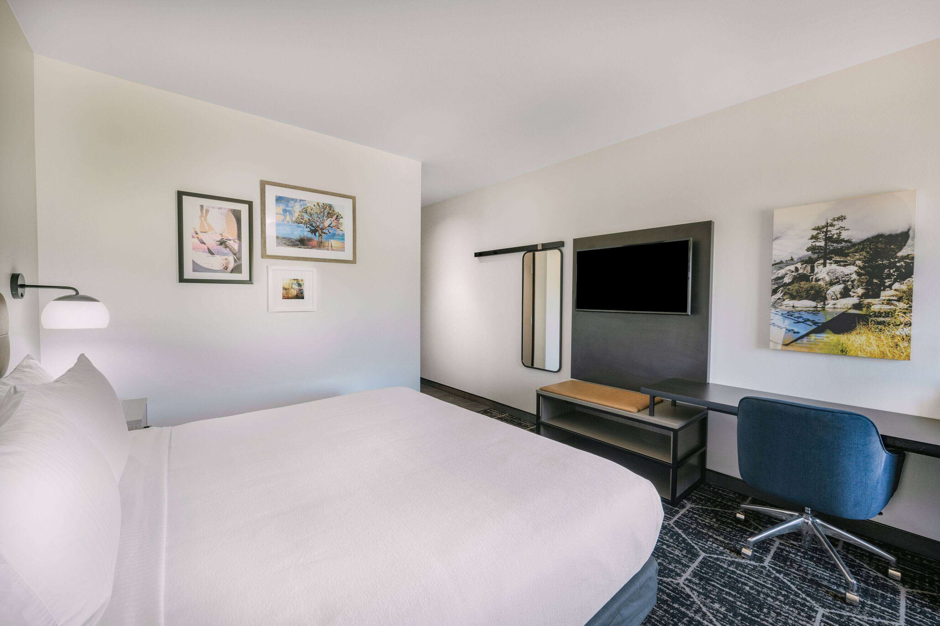Habitación de hotel con cama, escritorio, silla, televisión y dos cuadros en la pared.