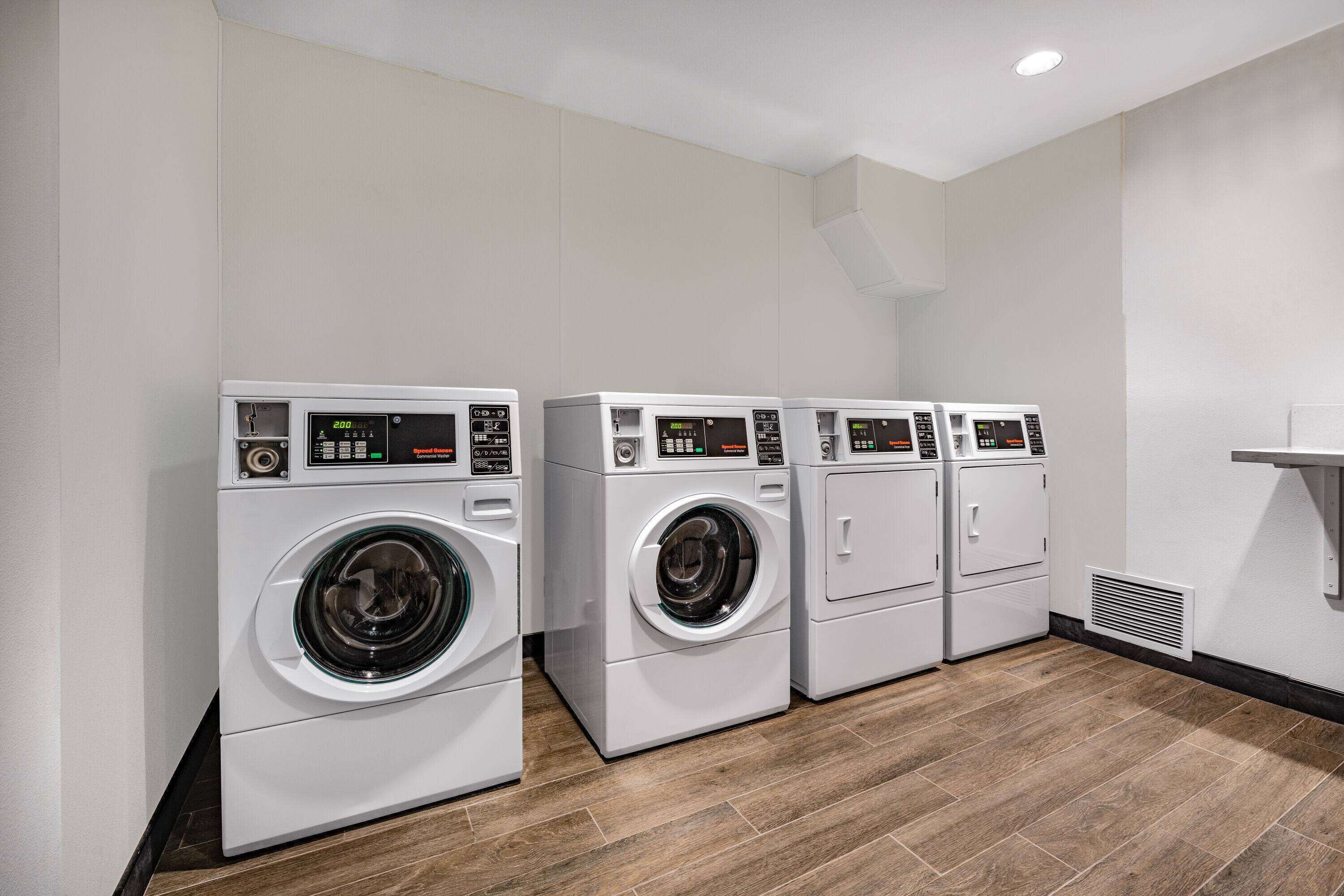 A laundry room with four stacked front-loading washing machines, a vent, and a wooden floor.