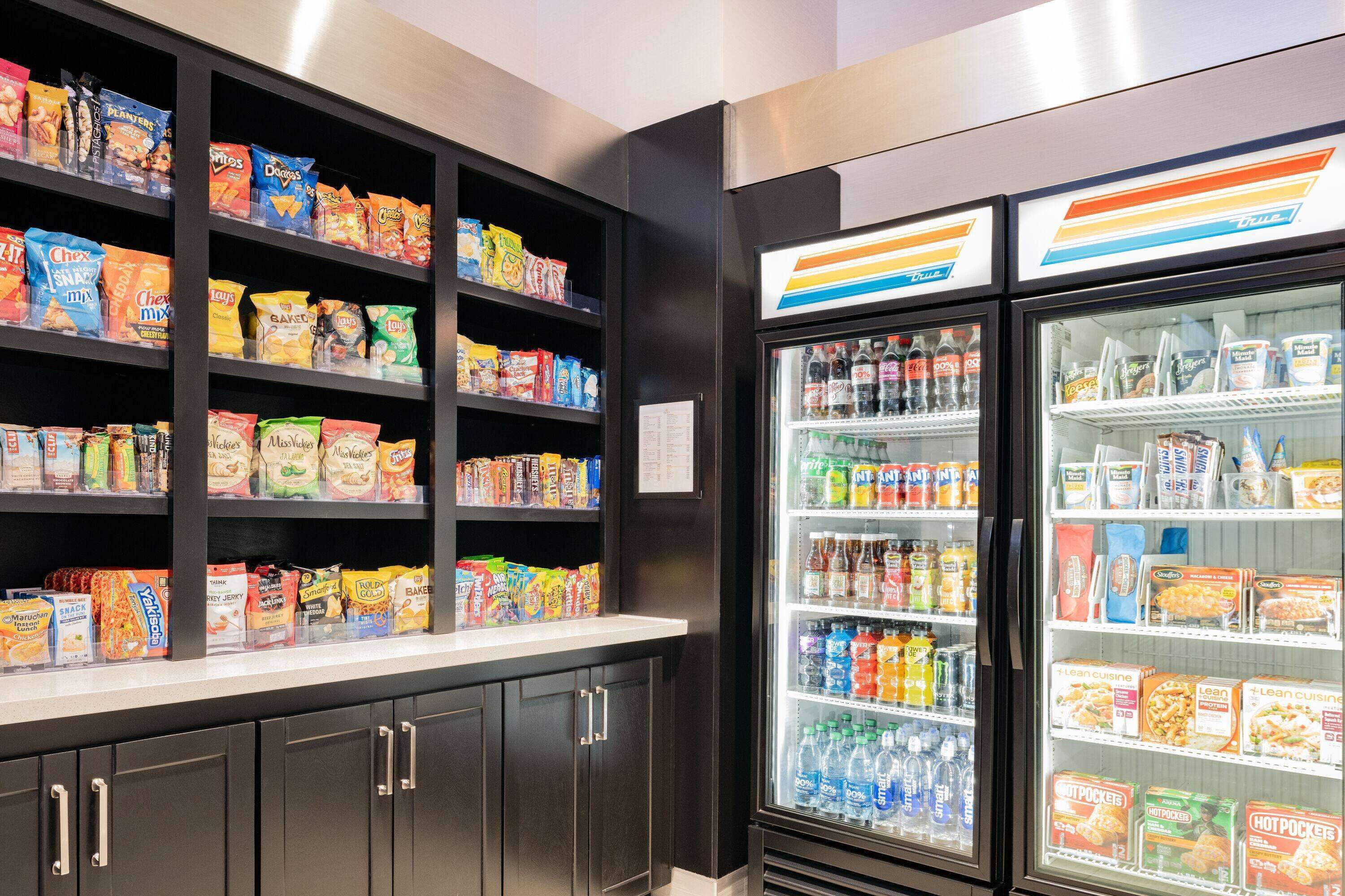 Een snack- en drankgedeelte met schappen vol met diverse snacks en een koelvitrine met flessen.'