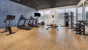 A modern gym with treadmills, an elliptical, a bench press, and dumbbells.