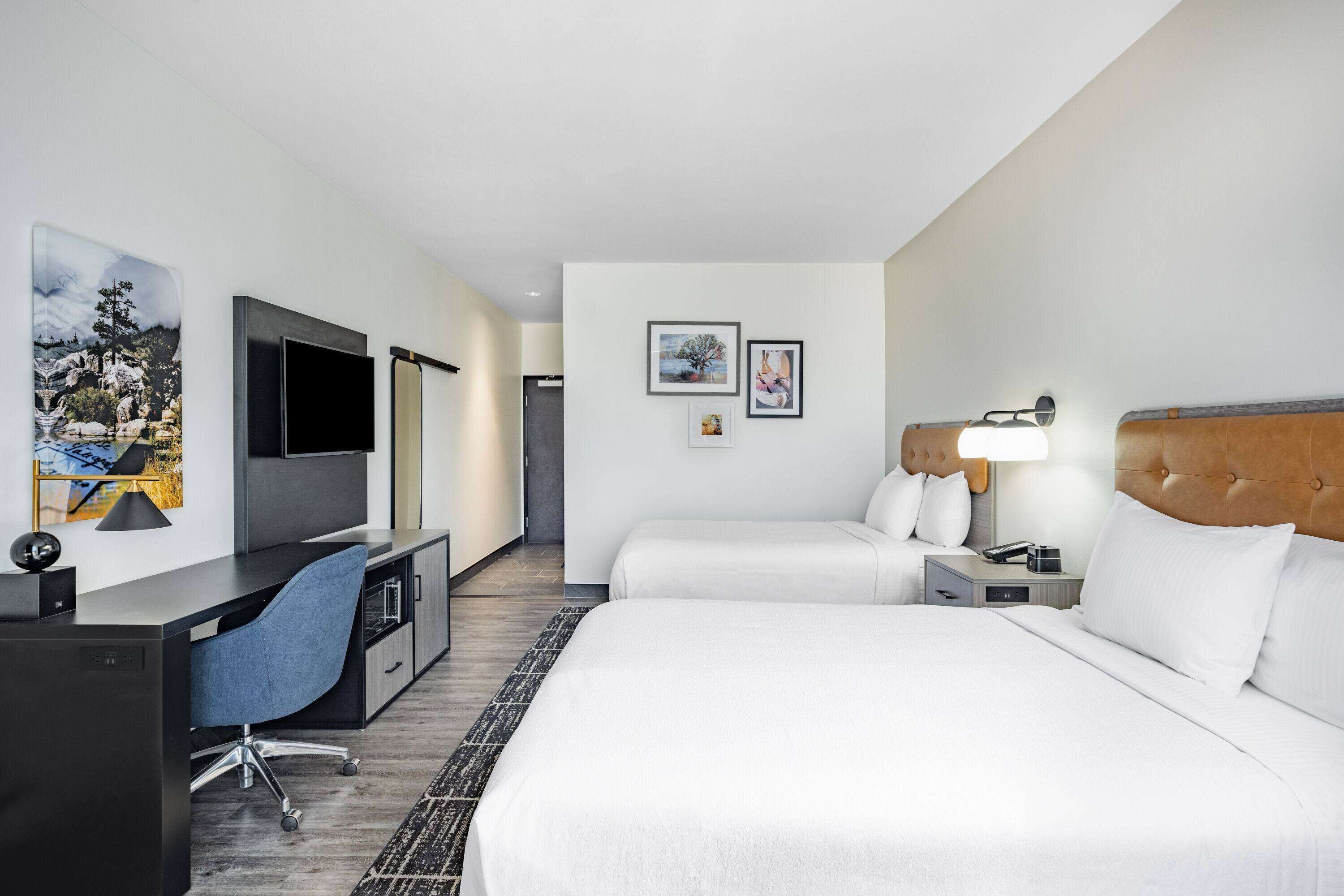A hotel room with a bed, a desk, a chair, a TV, and a nightstand.