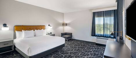 A hotel room with a large bed, a desk, a flat-screen TV, and a window with curtains.