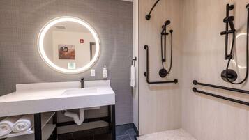 A modern bathroom with a white sink, a large mirror with a light, and a shower with black fixtures.