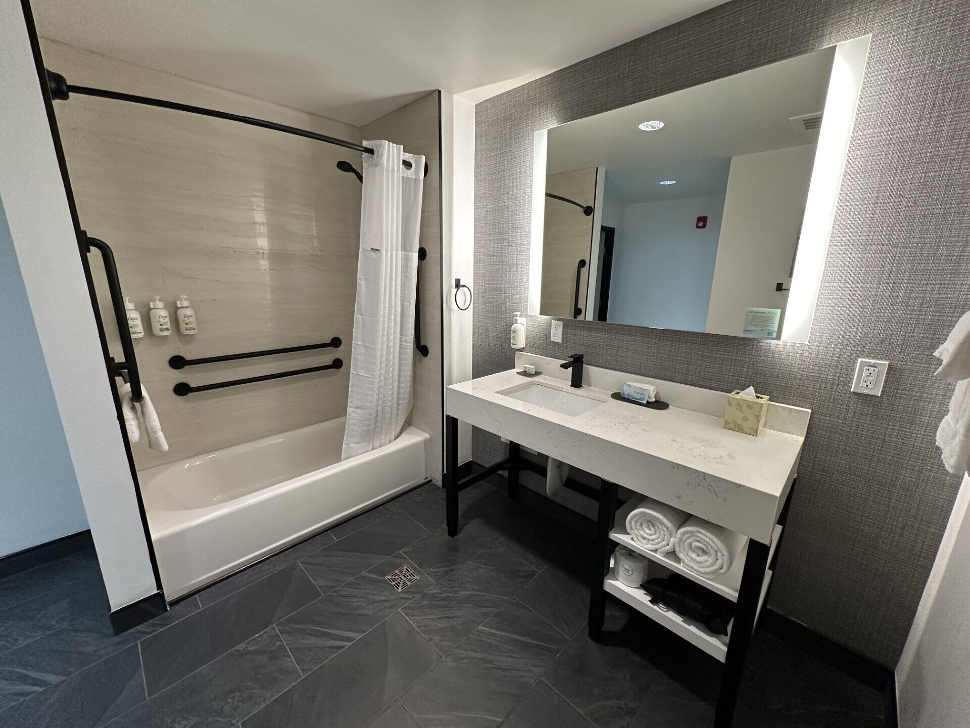 Un baño moderno con ducha a nivel, tocador con espejo y perchero.