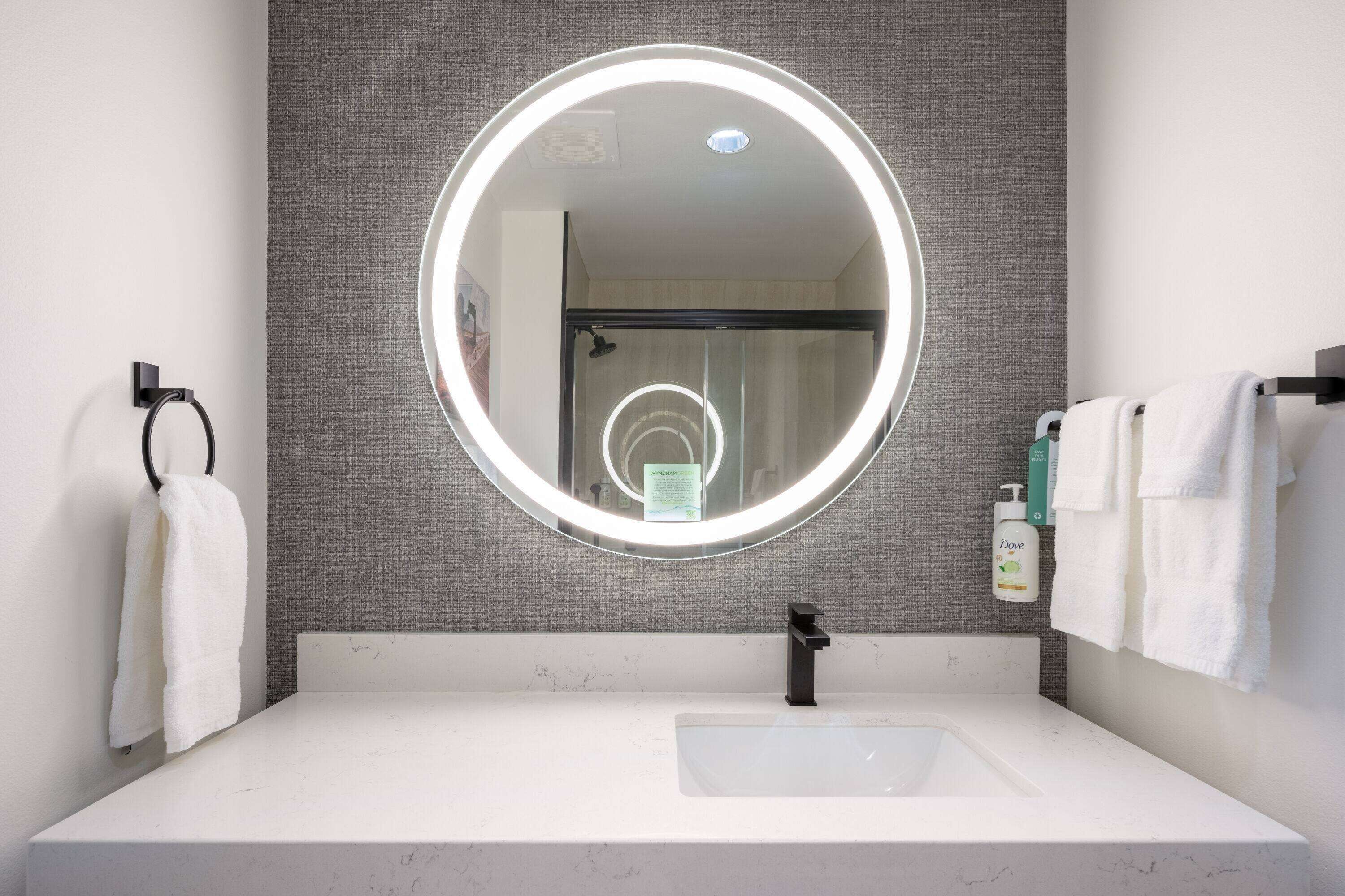 A modern bathroom with a round mirror, white sink, and towel rack.