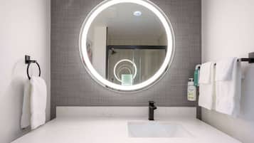 A modern bathroom with a round mirror, white sink, and towel rack.