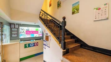 A hotel lobby with a reception desk, a staircase, and a bulletin board.