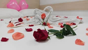 Una cama con pétalos de rosa y una rosa solitaria, almohadas y dos globos rosas.