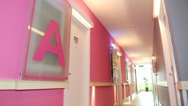 Um corredor com portas identificadas por letras, uma placa indicando uma área infantil e um corredor com um aparelho de iluminação.
