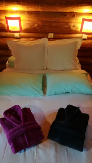 A bed with white pillows and a green blanket, two bedside lamps, and two folded towels.