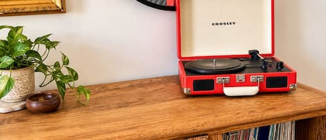 Un bureau en bois sur lequel se trouve une valise rouge contenant une platine, un tableau encadré, un miroir et une plante en pot.