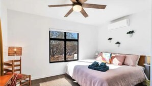 A bedroom with a bed, a ceiling fan, a window, a desk, and a chair.