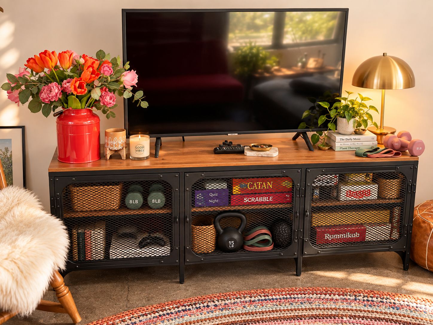 Un salon avec un téléviseur, un vase rouge rempli de fleurs, une bougie et du matériel de sport.