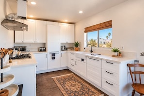 A modern kitchen with white cabinets, a gas stove, a microwave, and a window with a view of palm trees.