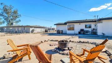 Une propriété située en bord de mer, dotée d’un patio avec des chaises en bois, un foyer et un petit bâtiment avec un balcon.