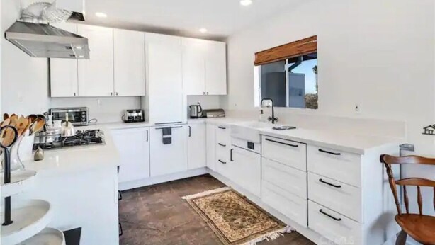 A modern kitchen with white cabinets, a gas stove, and a wooden-framed window.