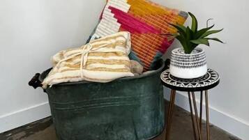 Un coin aménagé avec un banc recouvert d’un tissu vert, un plaid coloré en tissu tissé et une petite table sur laquelle est posée une plante en pot.