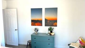 Une chambre avec une porte blanche, une commode turquoise, deux tableaux représentant des paysages, un globe terrestre et un petit tabouret.