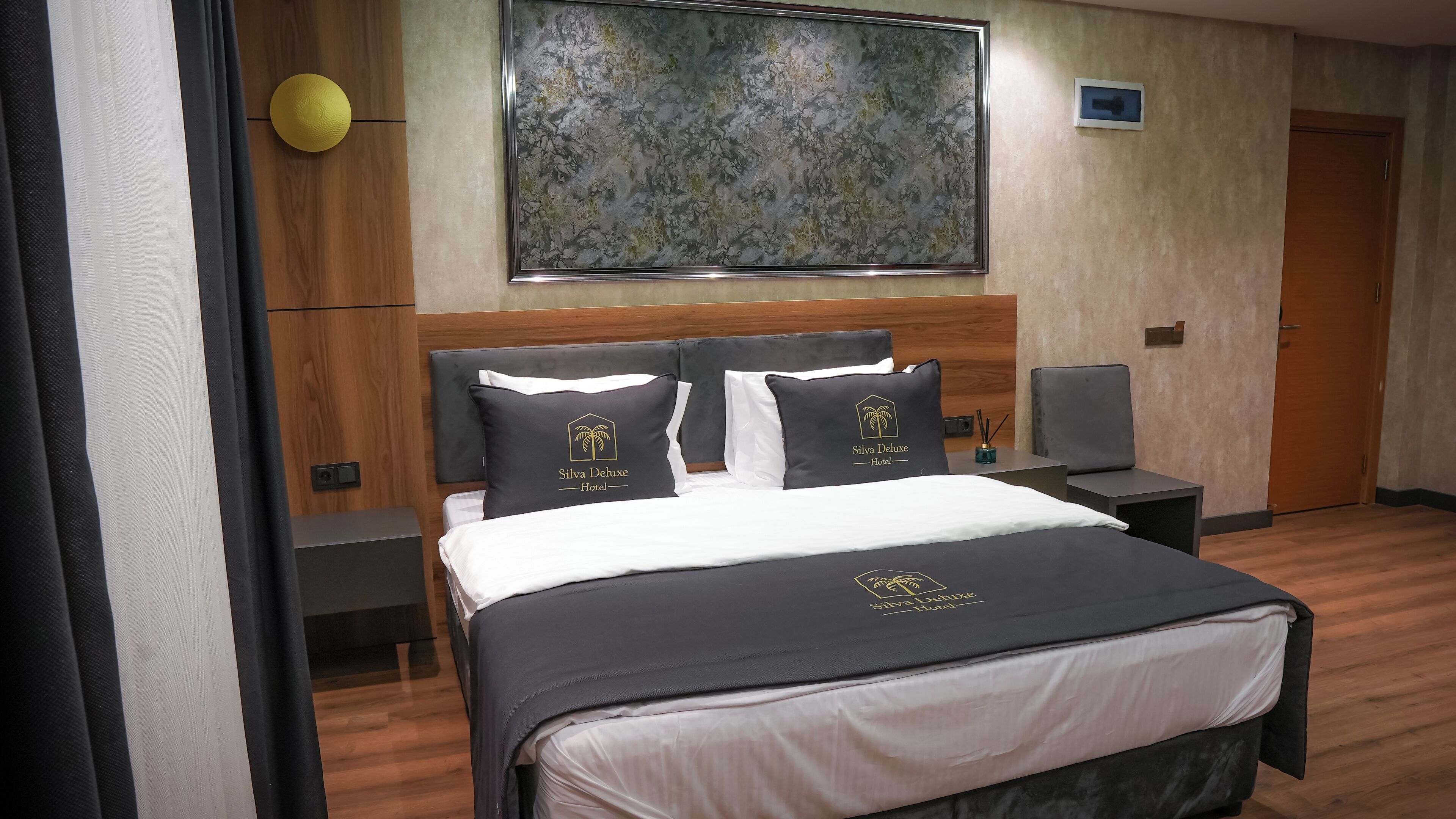 Habitación de hotel con cama, dos mesitas de noche, un escritorio, una silla, un cuadro en la pared y una puerta.