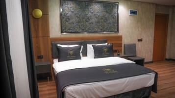 Habitación de hotel con cama, dos mesitas de noche, un escritorio, una silla, un cuadro en la pared y una puerta.