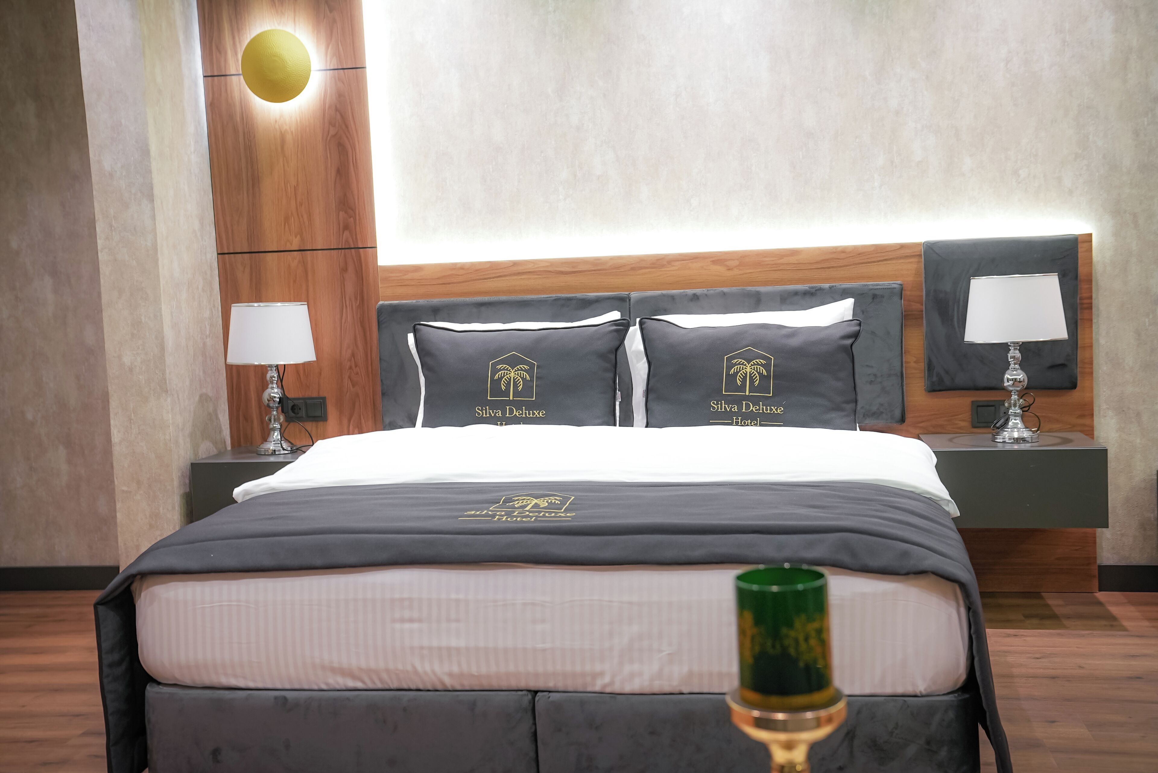 Habitación de hotel con una cama bien hecha, dos mesitas de noche con lámparas y un aplique en la pared.