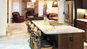 Une cuisine moderne dotée d’un îlot central, de tabourets de bar, d’un réfrigérateur et d’un mur d’accent en pierre.
