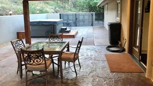 Une terrasse extérieure avec une table et des chaises à plateau en verre, un jacuzzi et un espace abrité offrant une vue sur le jardin arrière.