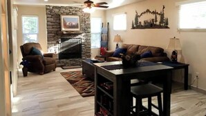 Un salon avec une cheminée en pierre, un ventilateur de plafond, un canapé, une table basse et une bibliothèque.
