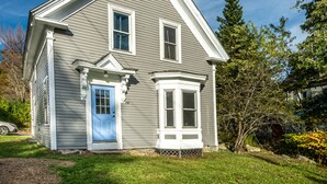A two-story house with a blue front door, a bay window, and a small porch.