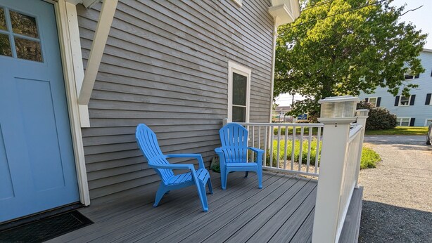 A wooden deck with two blue Adirondack chairs and a white railing.