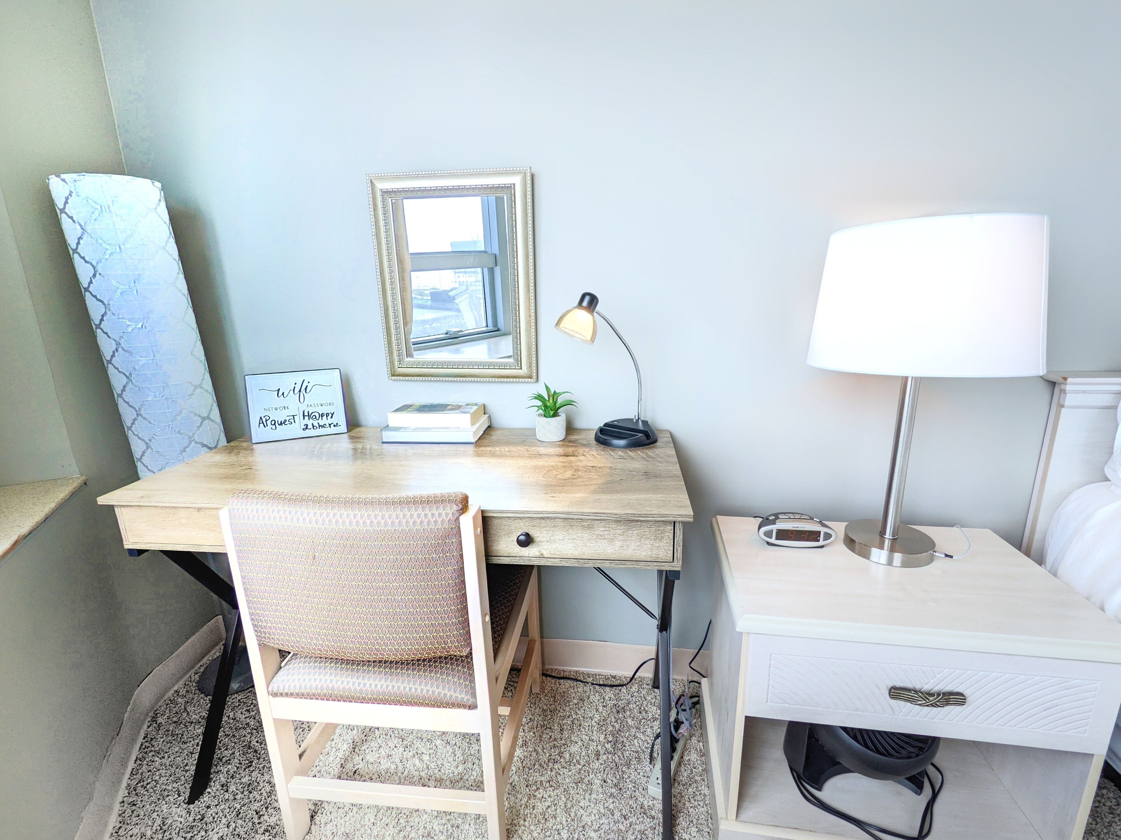 Ein ordentlich eingerichteter Arbeitsbereich mit Schreibtisch, Stuhl, Lampe und Nachttisch mit Lampe.