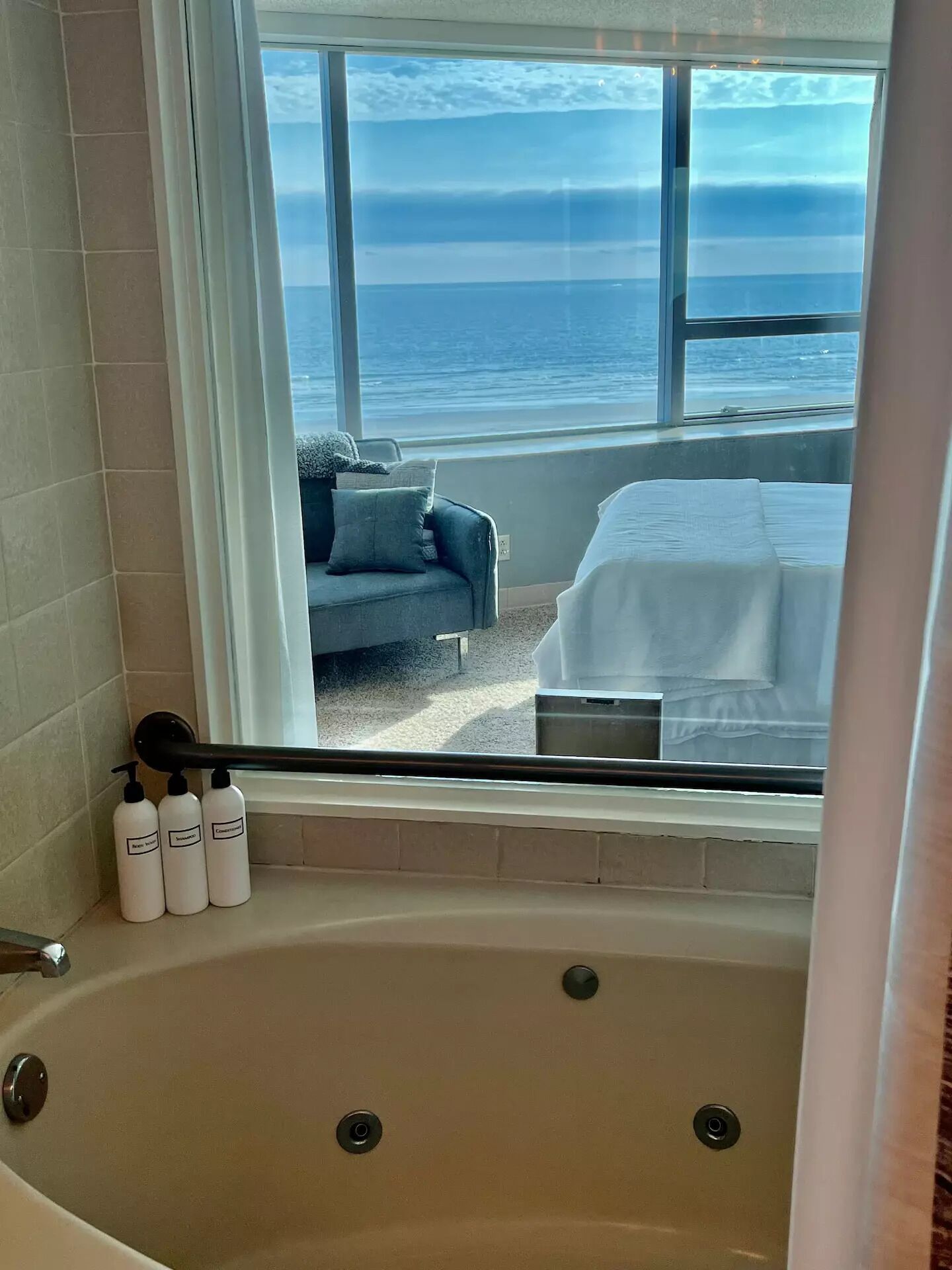 A bathroom with a bathtub, a window with a view of the ocean, and toiletries on the side.