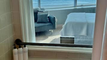 A bathroom with a bathtub, a window with a view of the ocean, and toiletries on the side.