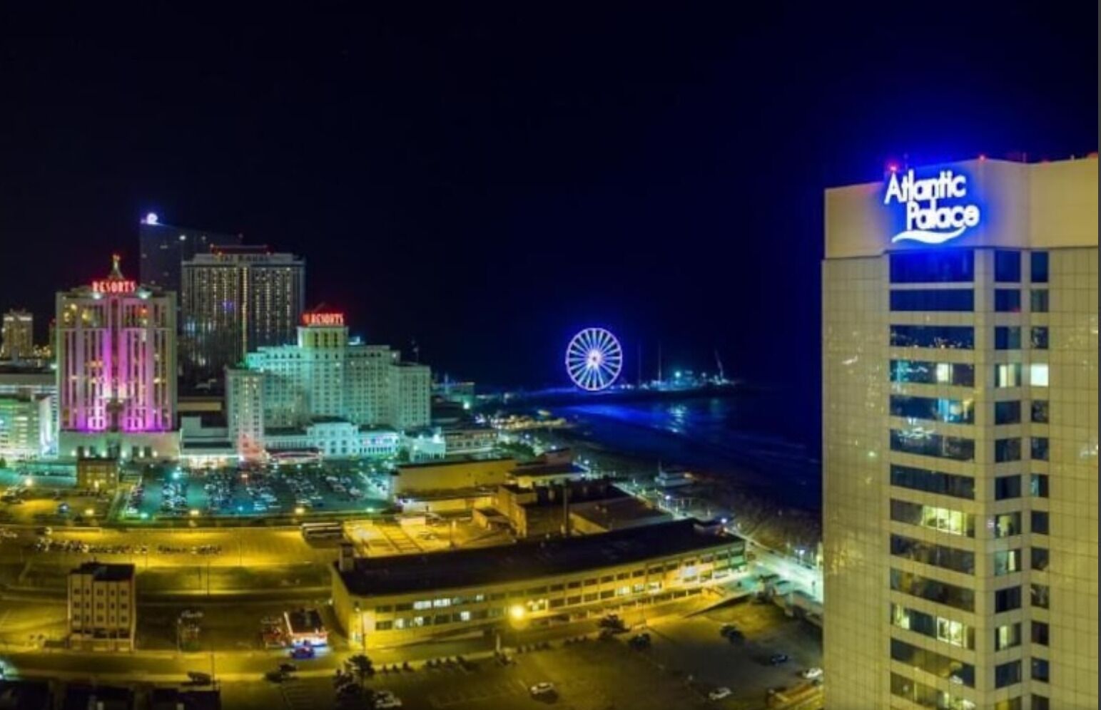Une vue nocturne d’une ville, avec un grand bâtiment de casino bien visible, une grande roue et un hôtel appelé « Atlantic Palace ».