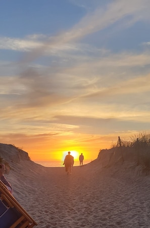 Solnedgang over en sandstrand med klitter.