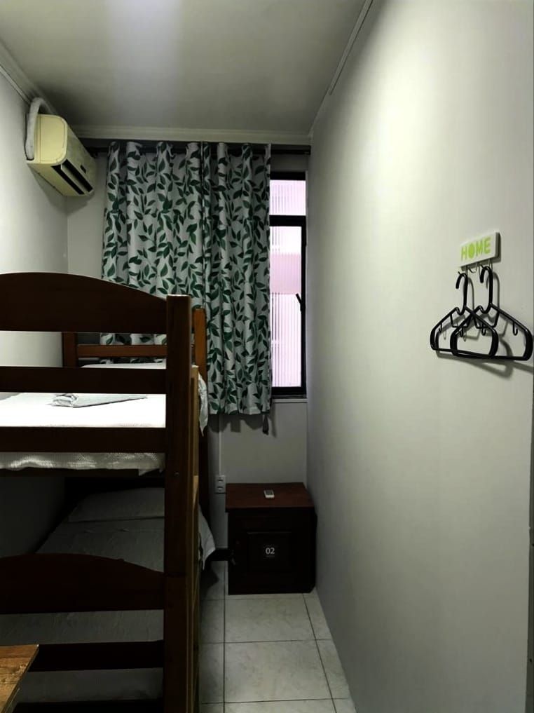 A small room with a bunk bed, a desk, a chair, a heater, a window with curtains, and a coat rack.
