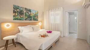 A bedroom with a bed, a bedside table, a window with curtains, and a wall with three paintings.