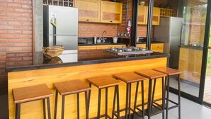 Une cuisine moderne avec un mur en briques, des armoires en bois, un réfrigérateur en acier inoxydable et un coin bar avec des tabourets.