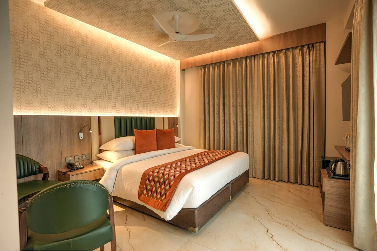 A hotel room with a large bed, a desk with a telephone, a chair, and a view of the outside through curtains.